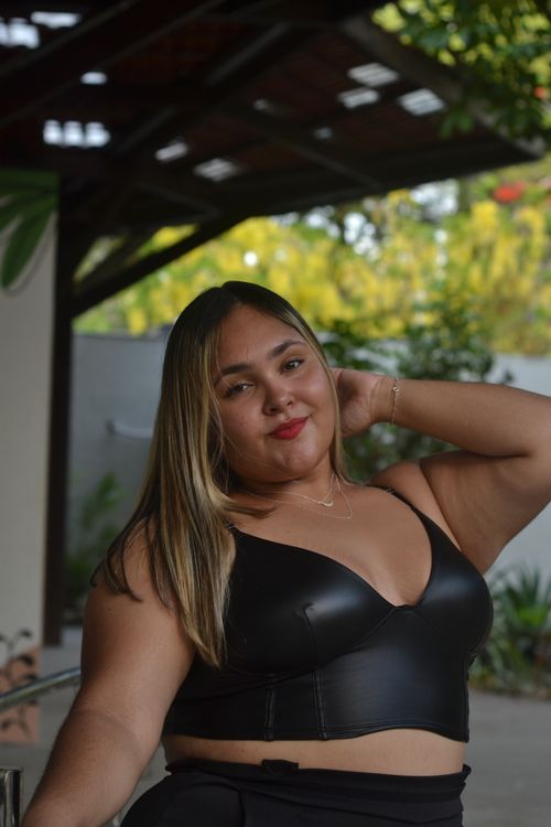 Free Confident young woman posing in a black top, enjoying an outdoor setting with lush greenery. Stock Photo
