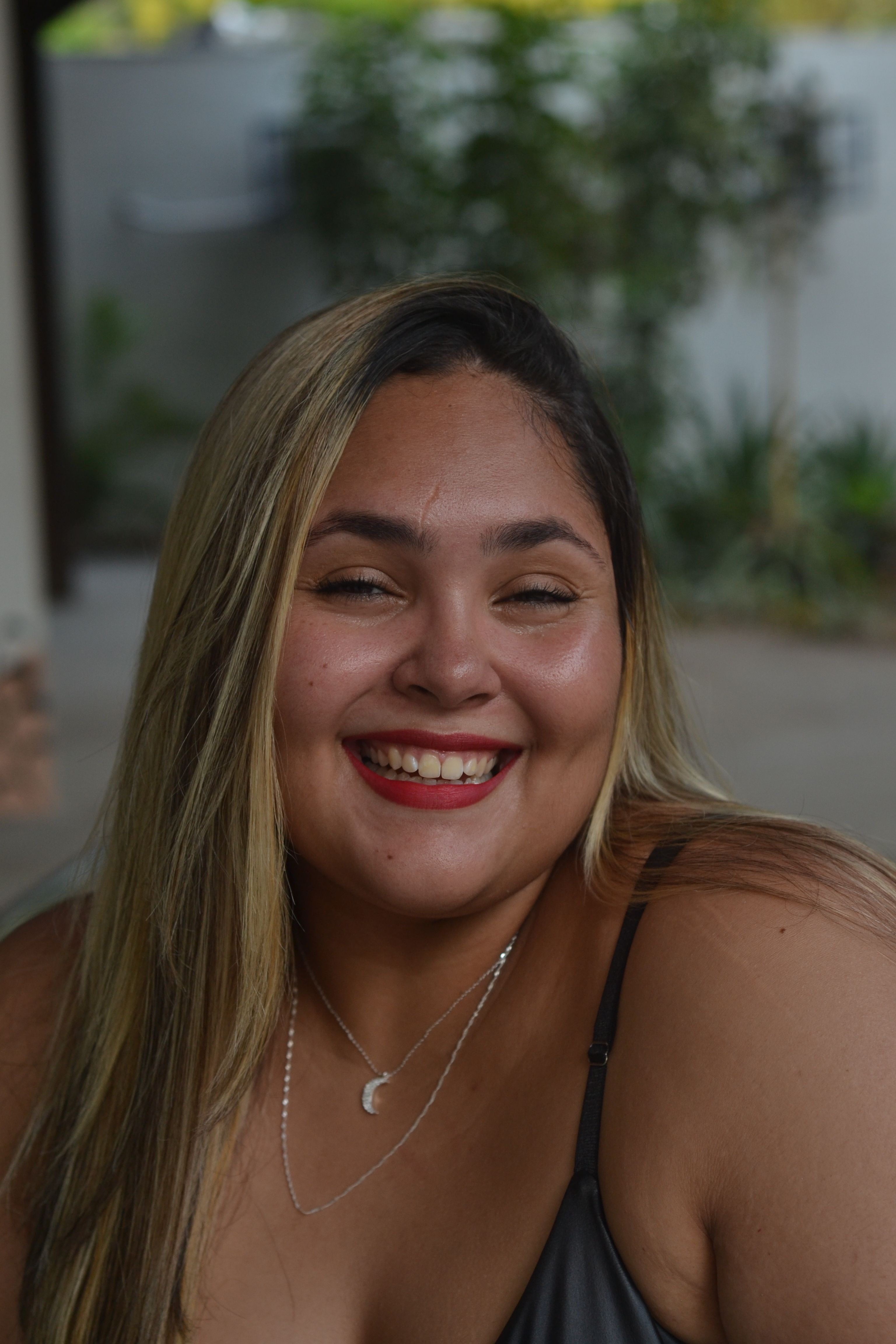 Portrait of a smiling young woman outdoors with a summer backdrop.