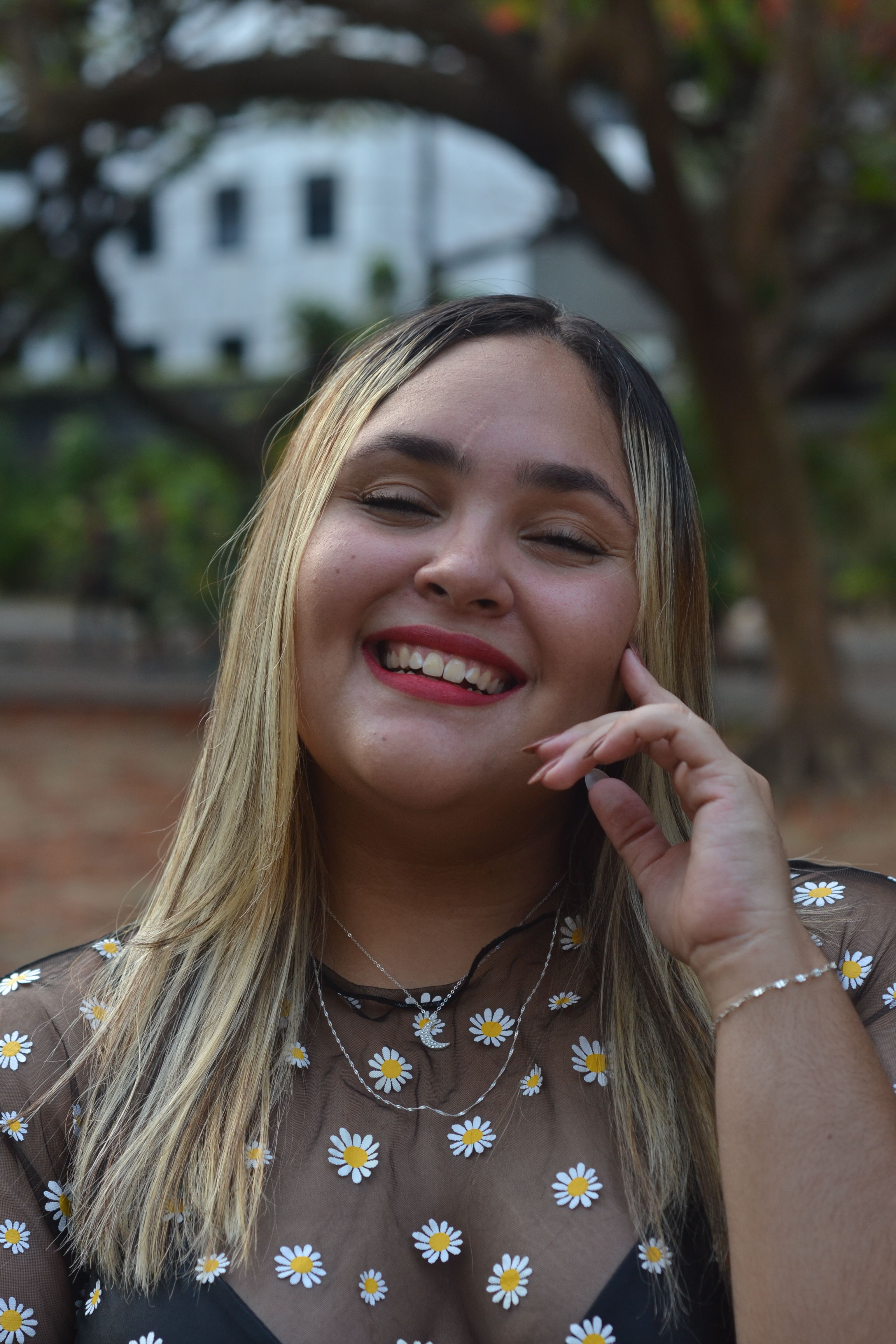 Smiling young woman with daisy-patterned top enjoying a sunny day outdoors.