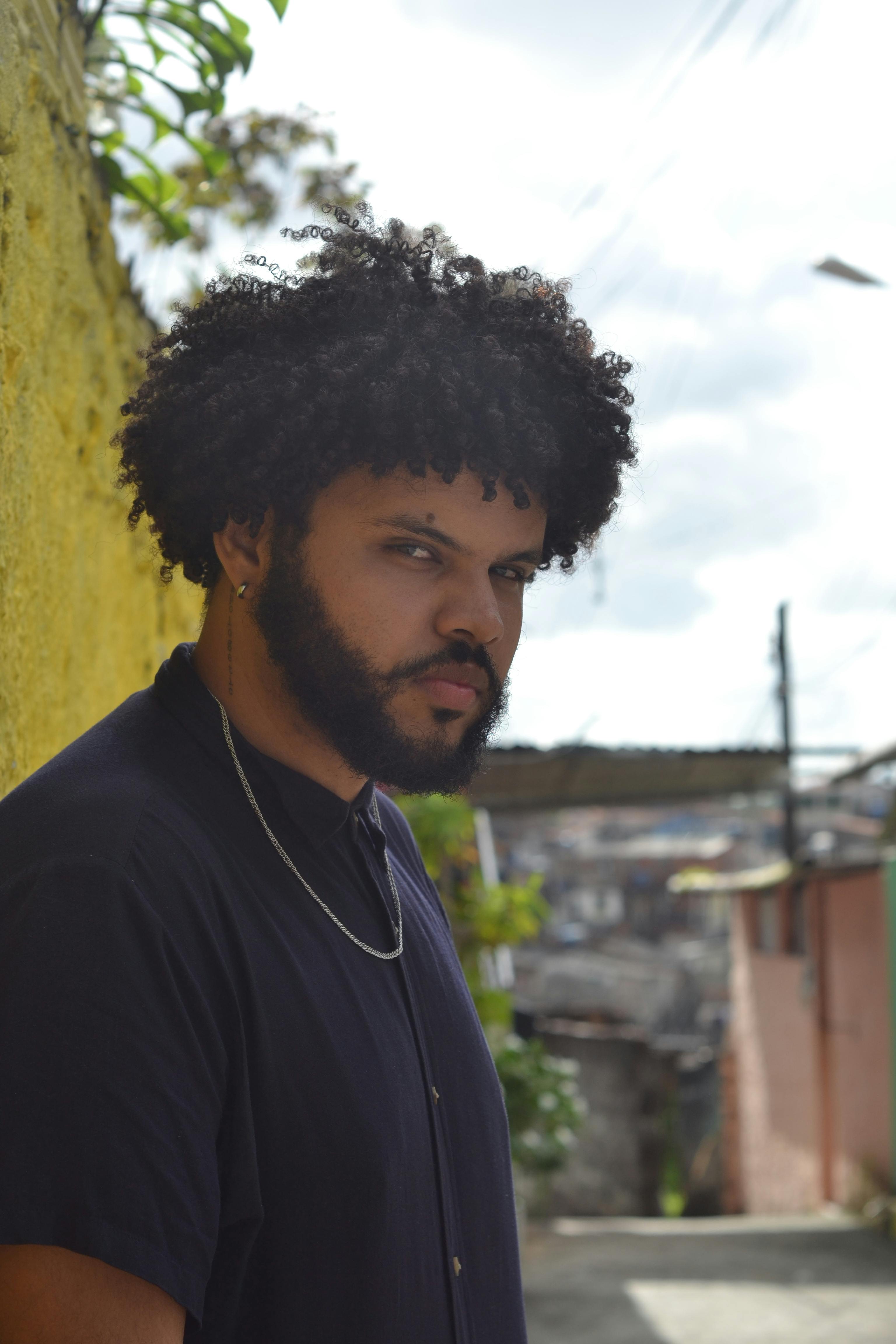 Confident man poses beside a vibrant yellow wall in an urban setting.