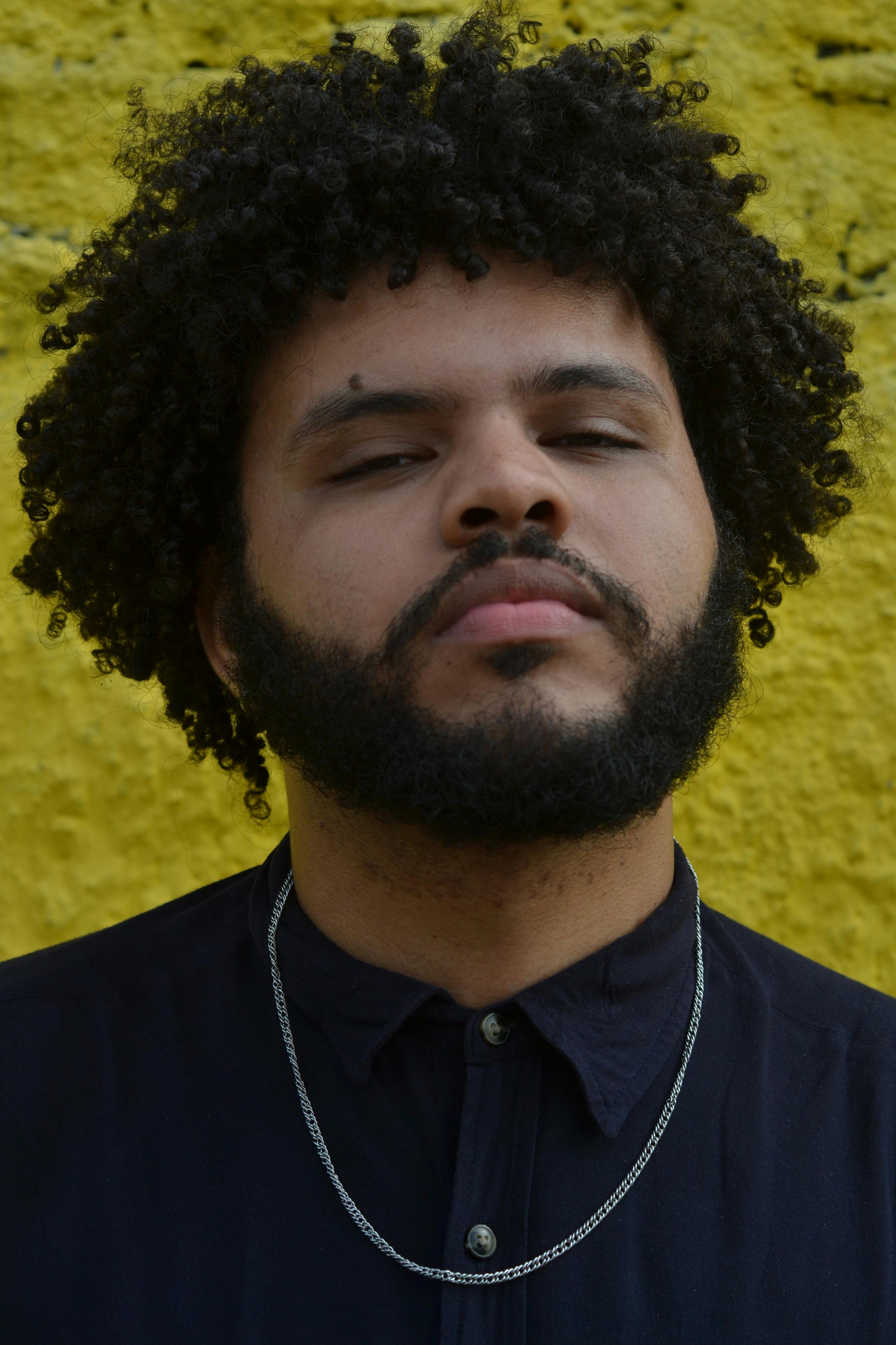 Portrait of a man with curly hair and beard against a vibrant yellow background.