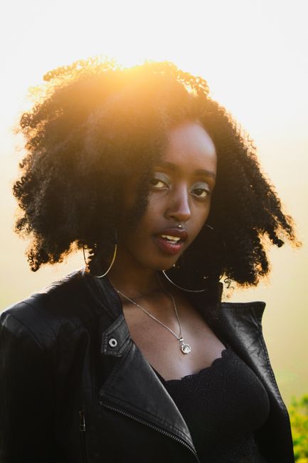 Portrait of African woman with afro hair, hoop earrings, and leather jacket in sunlight.