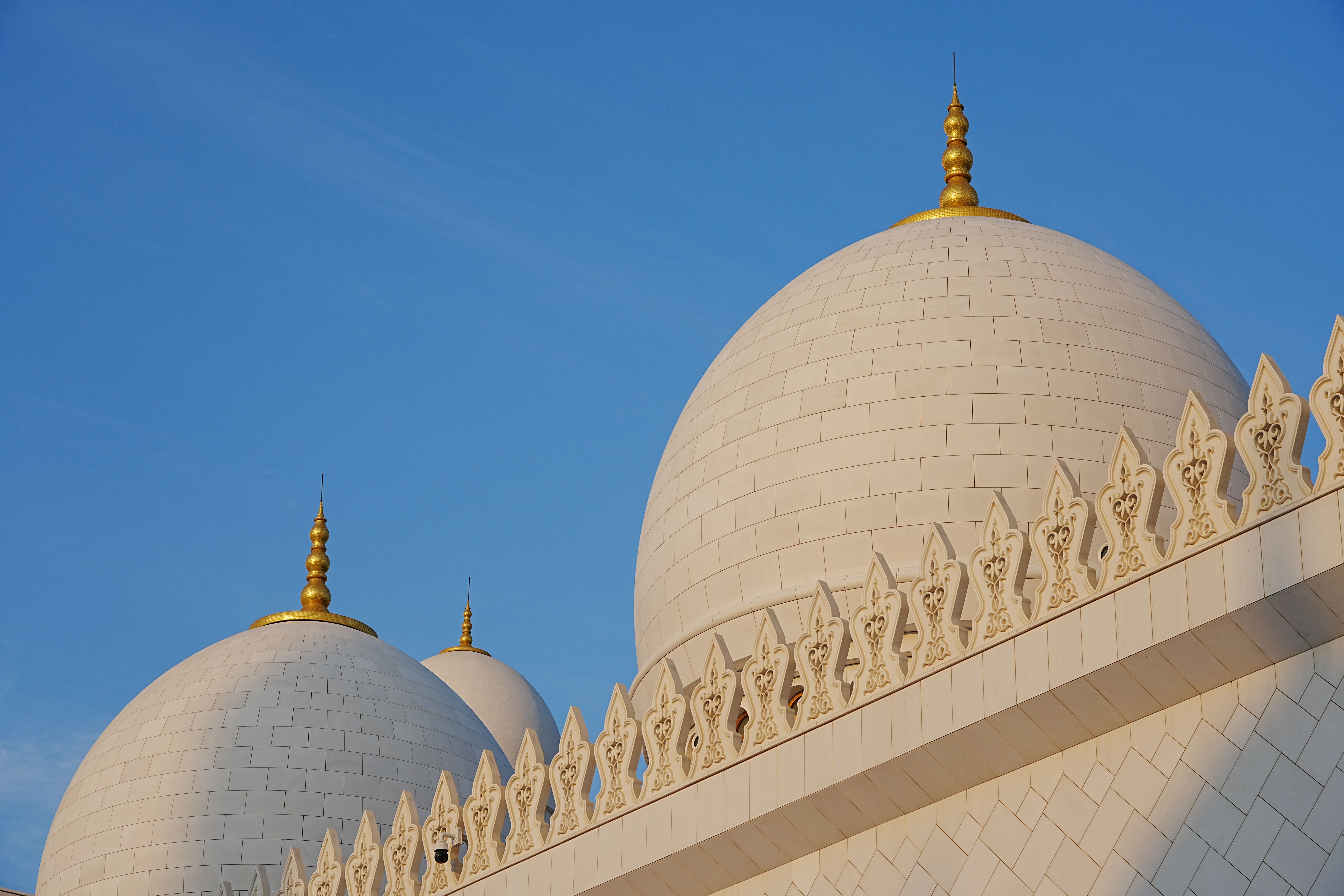 Close-up of the iconic domes of Sheikh Zayed Grand Mosque in Abu Dhabi against a clear blue sky.