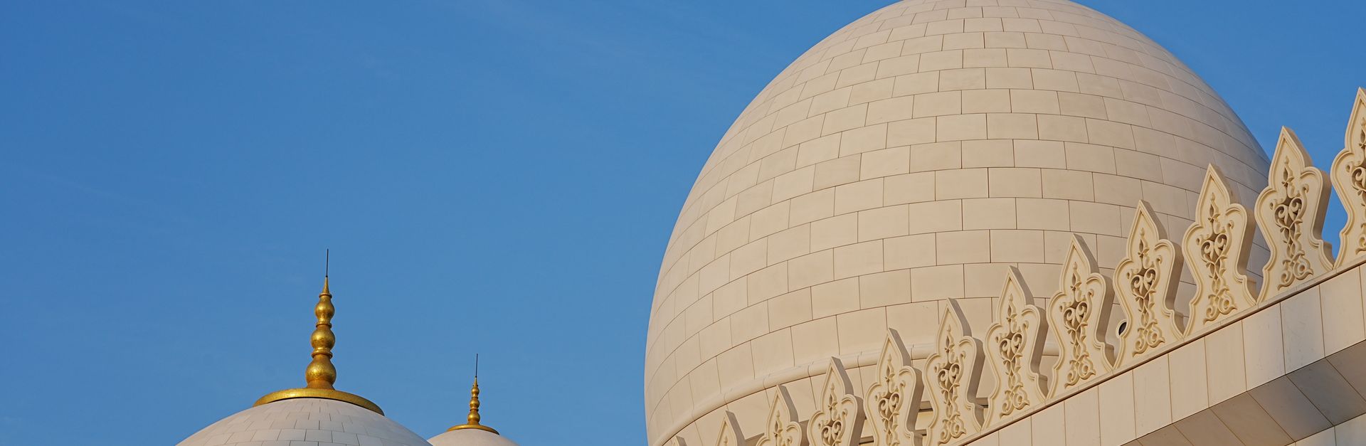 Close-up of the iconic domes of Sheikh Zayed Grand Mosque in Abu Dhabi against a clear blue sky.