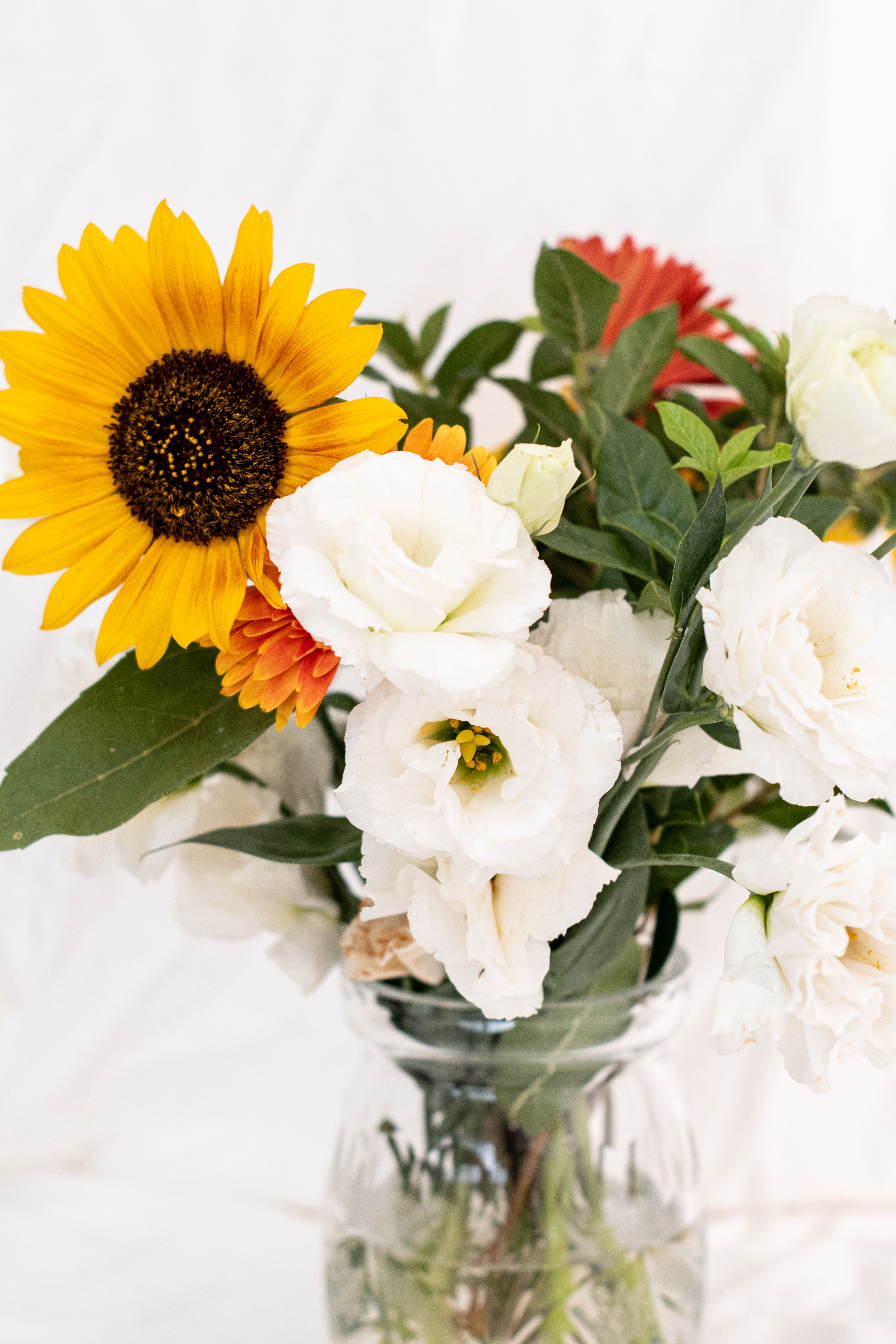 Bright bouquet featuring sunflower, white roses, and greenery in a glass vase.