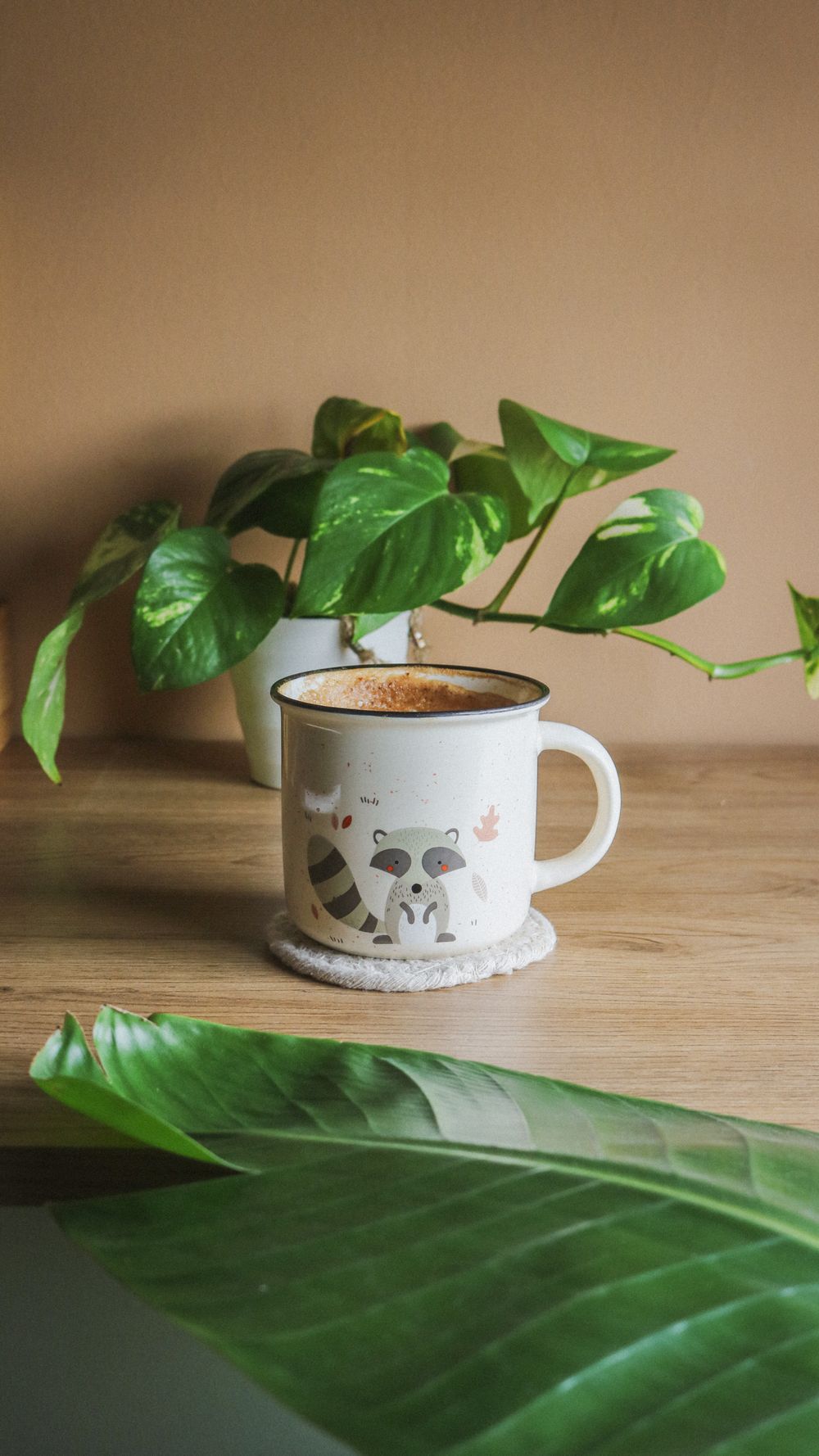 Une tasse de café décorée et une plante verte luxuriante sur une table en bois, ambiance chaleureuse.