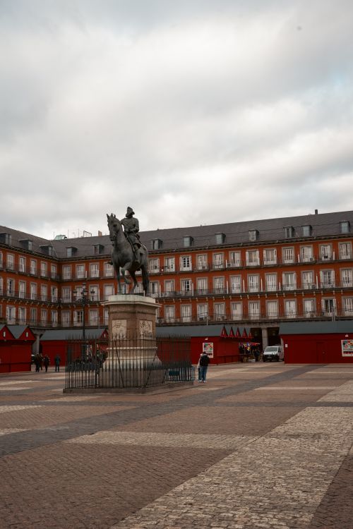 Free A historic plaza featuring an equestrian statue with traditional architecture on a cloudy day. Stock Photo