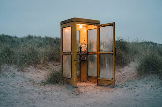 An illuminated vintage phone booth stands alone on Sankt Peter-Ording's sandy dunes.