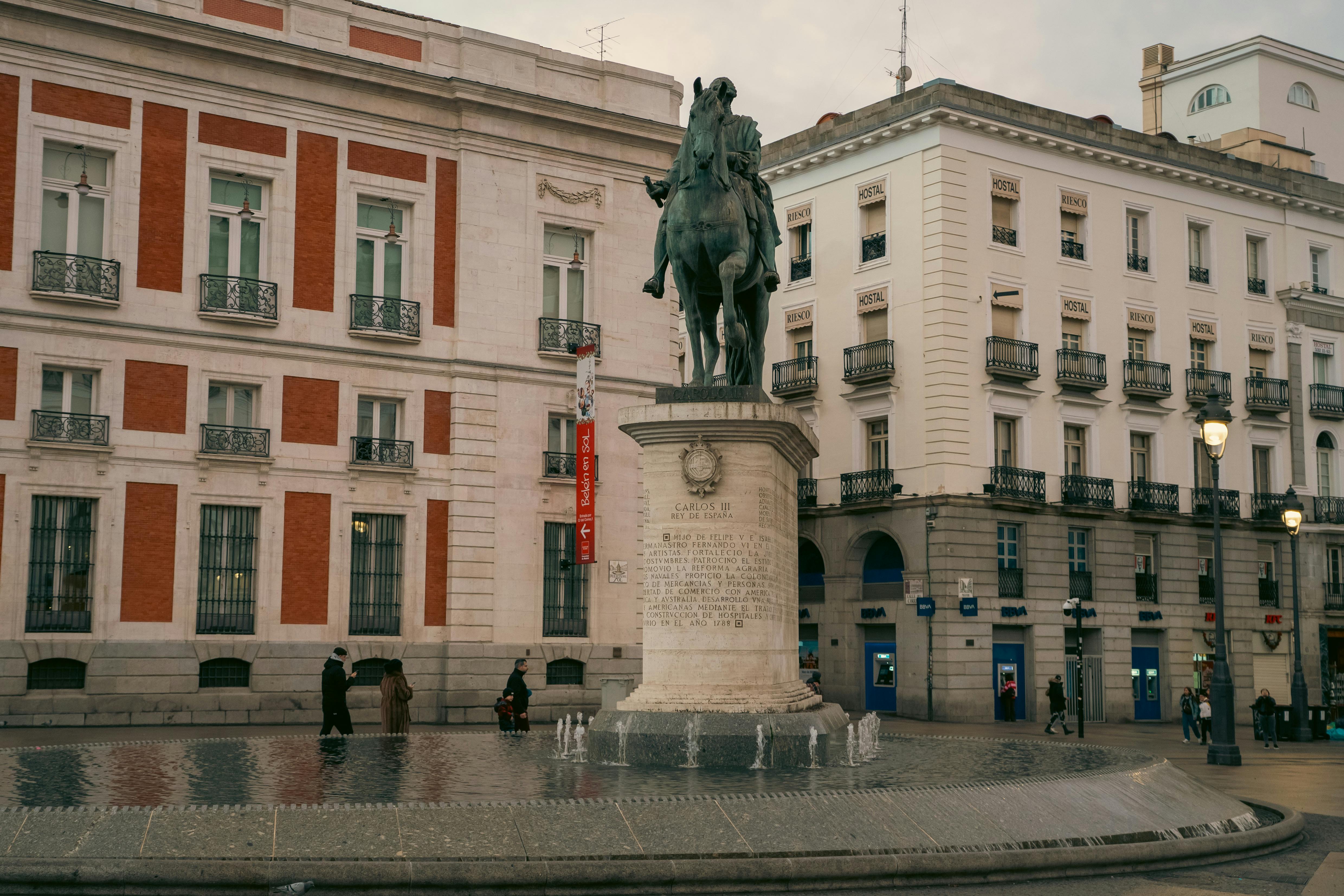 Equestrian statue in vibrant Madrid plaza with classic architecture and people. - Isla del Sol