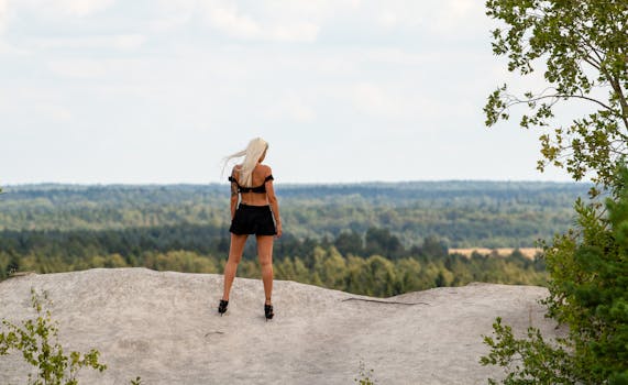 A blonde woman stands on a cliff in Vasalemma, Estonia, enjoying the vast forest view.