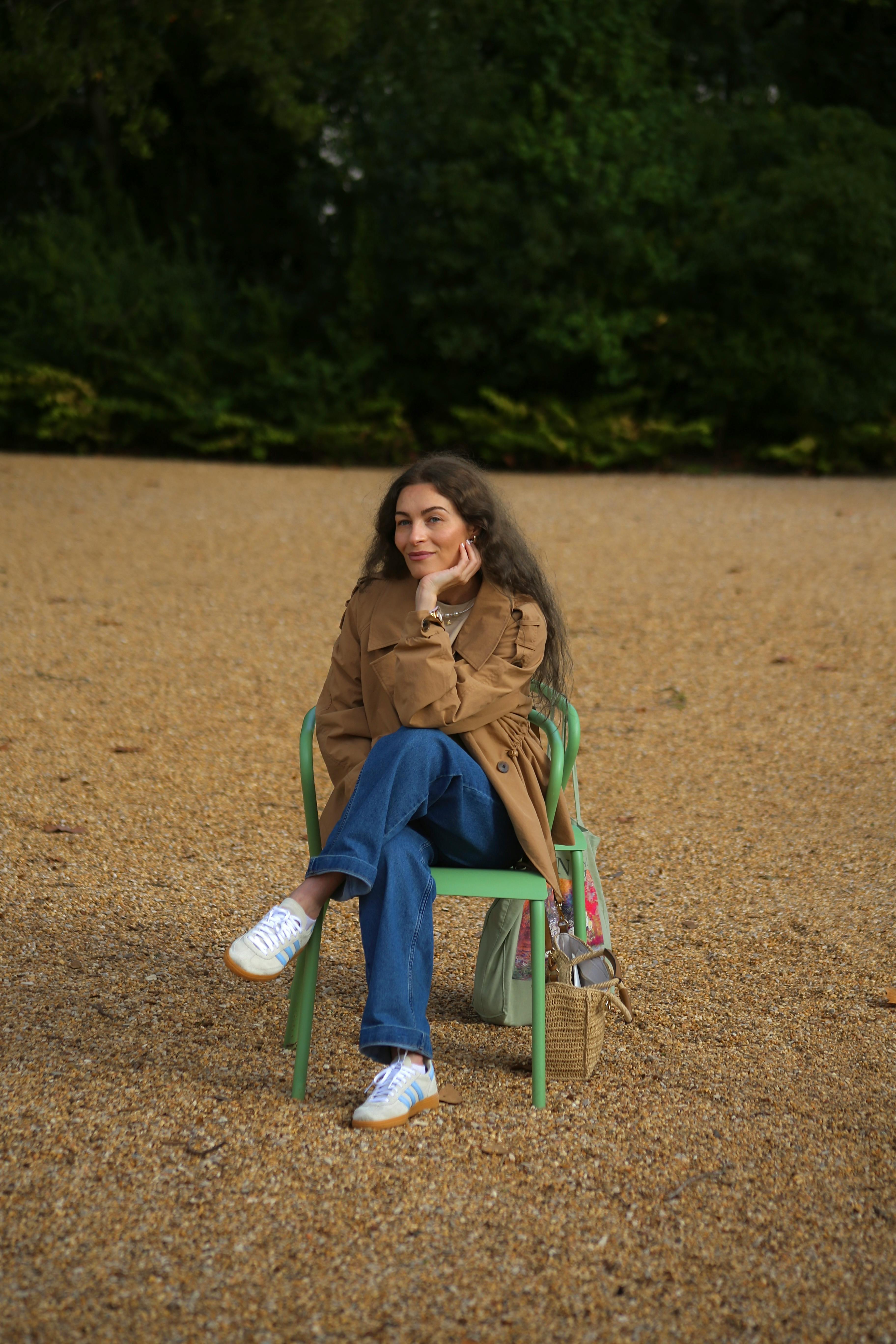 A woman in a brown jacket sits comfortably on a chair in a park in Lisboa, Portugal.