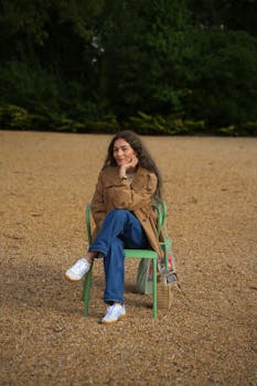A woman in a brown jacket sits comfortably on a chair in a park in Lisboa, Portugal.
