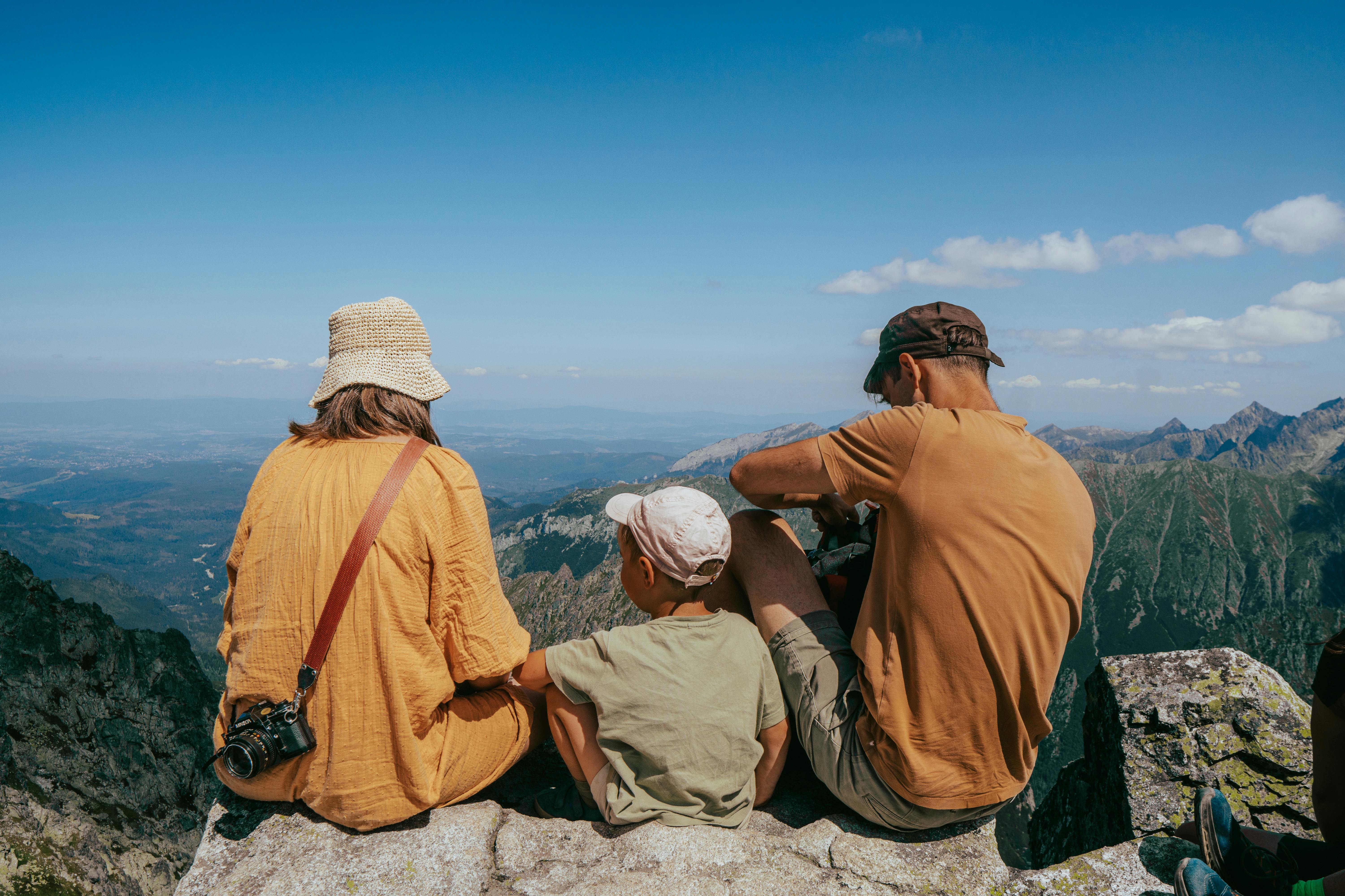 Family sitting on a rock, enjoying a panoramic view of the Tatra Mountains under clear blue skies.