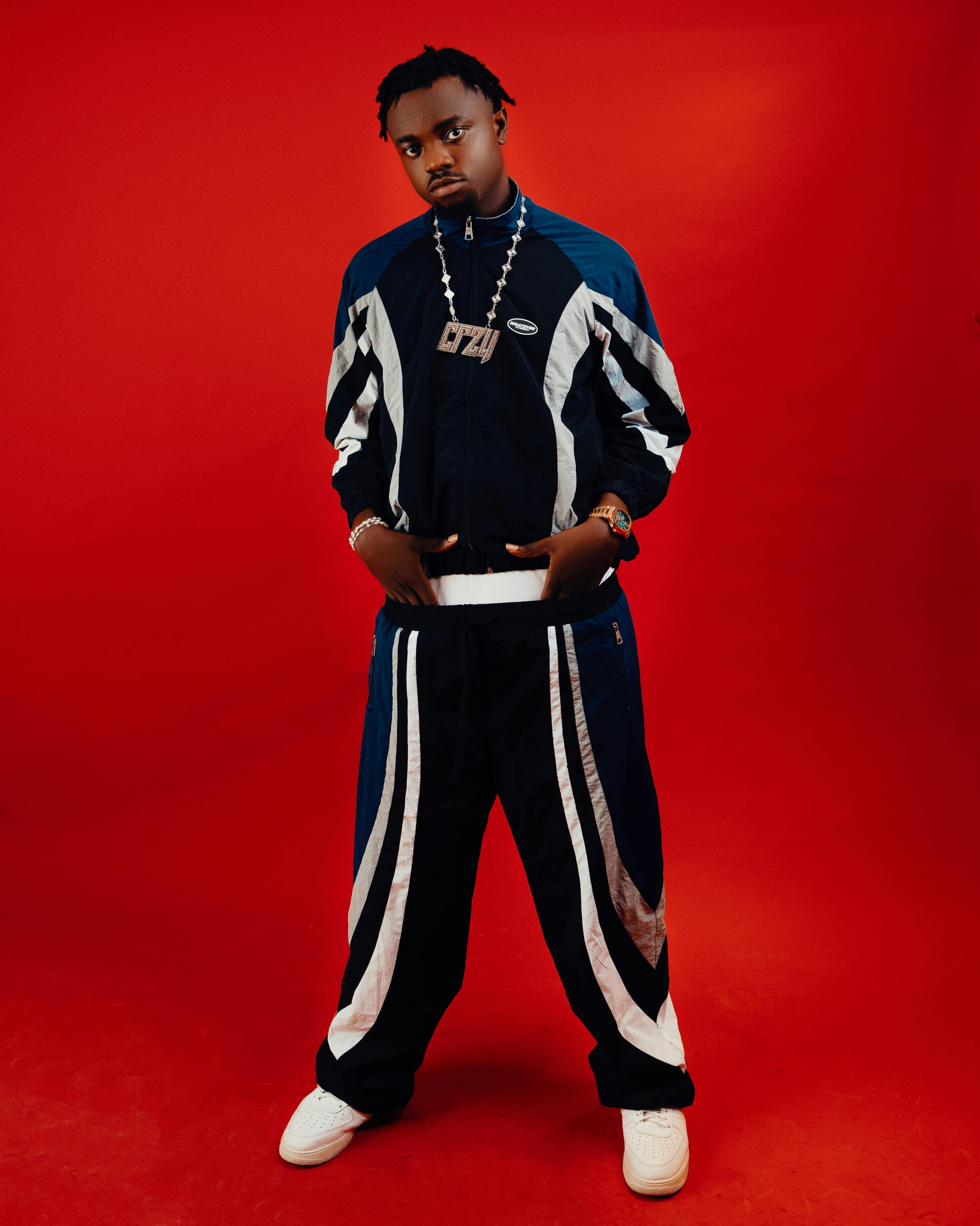 Confident young man poses in a stylish tracksuit against a bold red background.