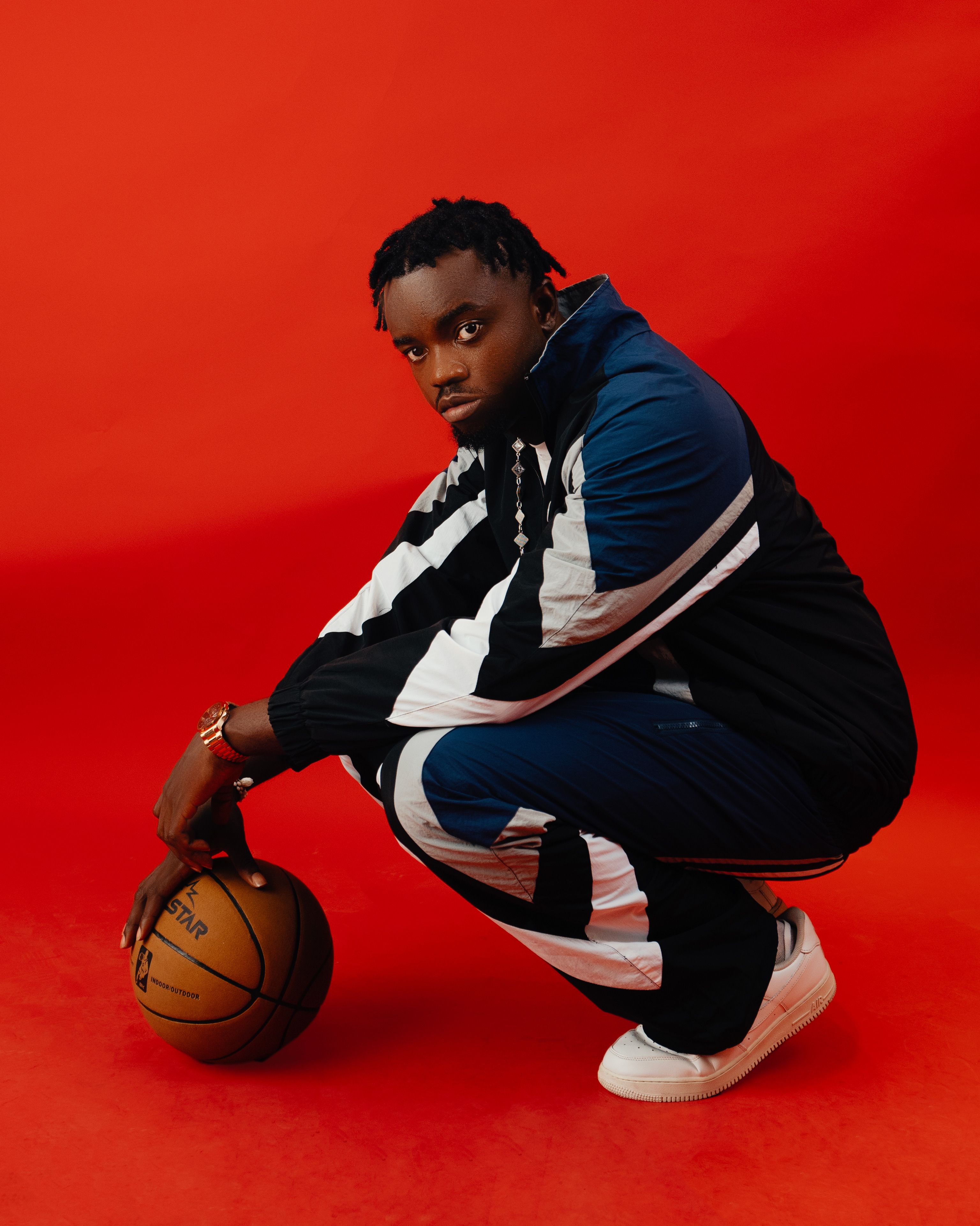 Stylish young man in tracksuit posing with basketball, set against a vivid red background.