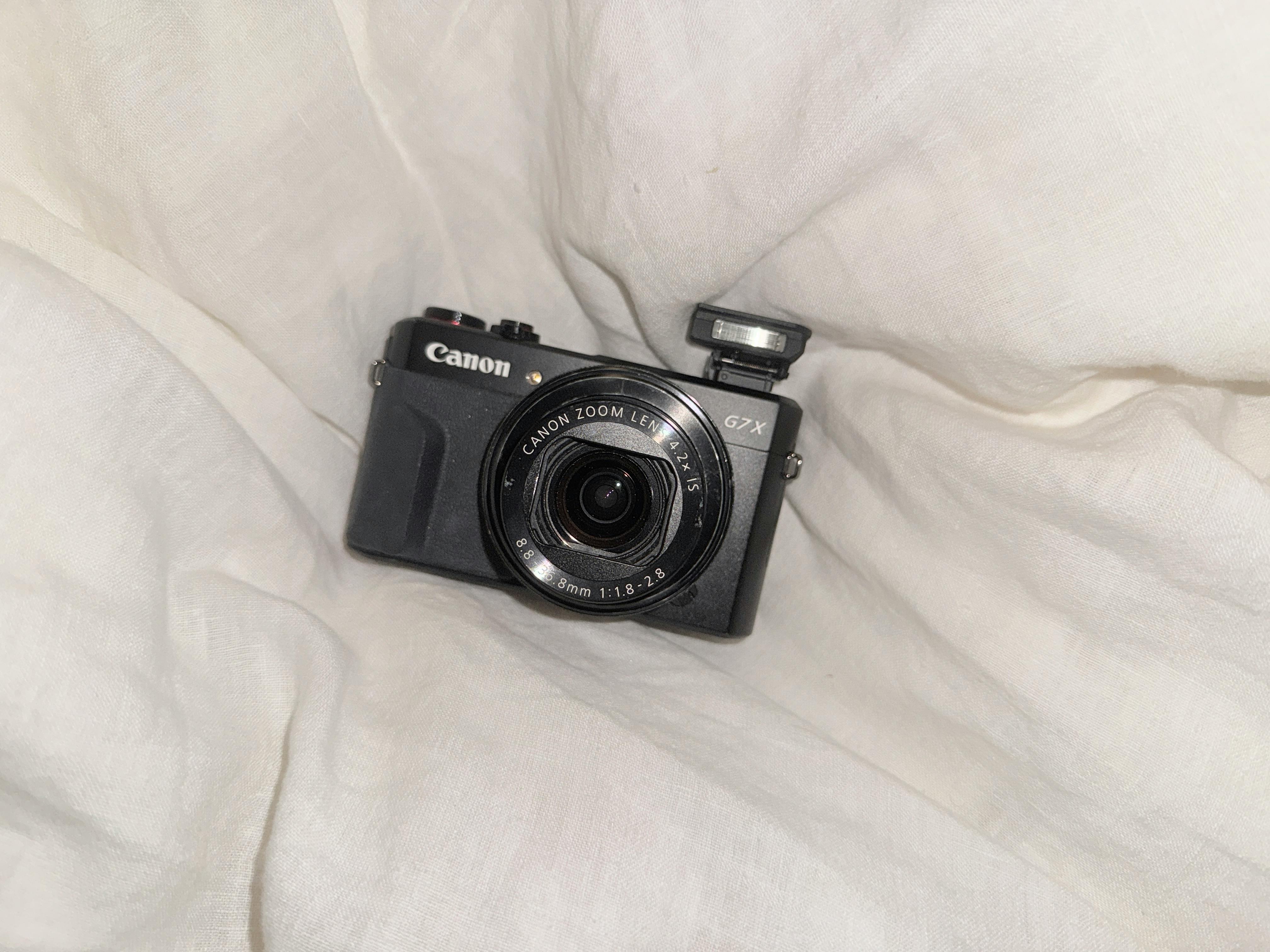 Compact digital camera with pop-up flash on soft white fabric, perfect for photography themes.