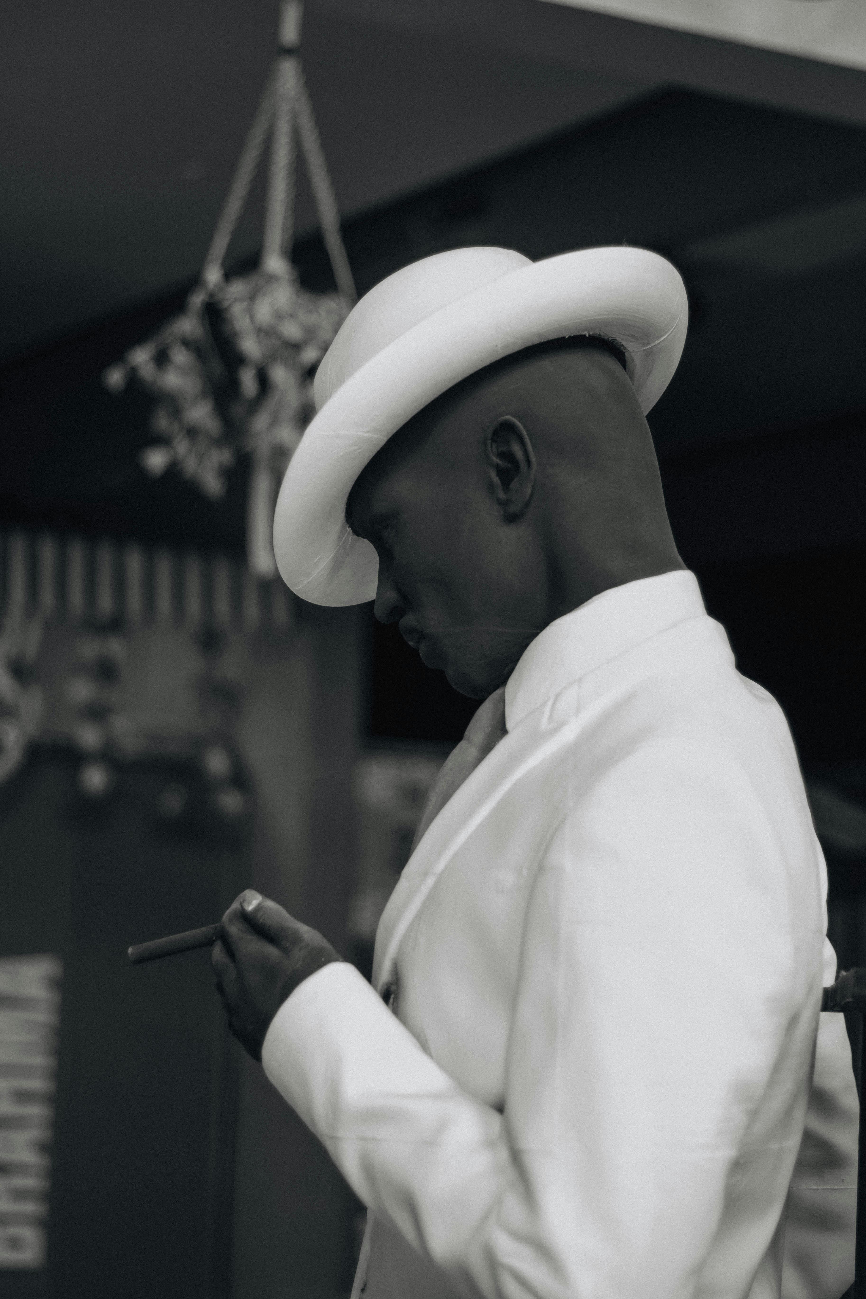 免費 一張時尚的黑白照片，照片中一位男士身穿白色西裝，戴著禮帽，手持雪茄。 圖庫相片