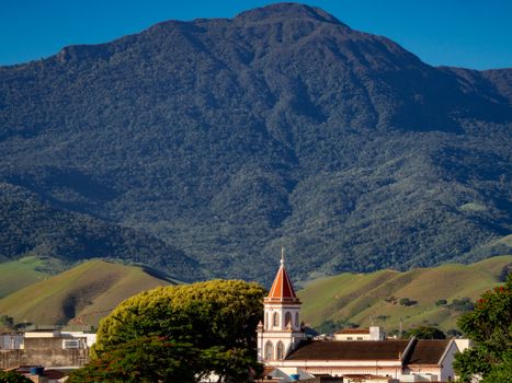 Vue panoramique de Cruzeiro avec ses montagnes luxuriantes et son clocher emblématique se détachant sur un ciel dégagé.
