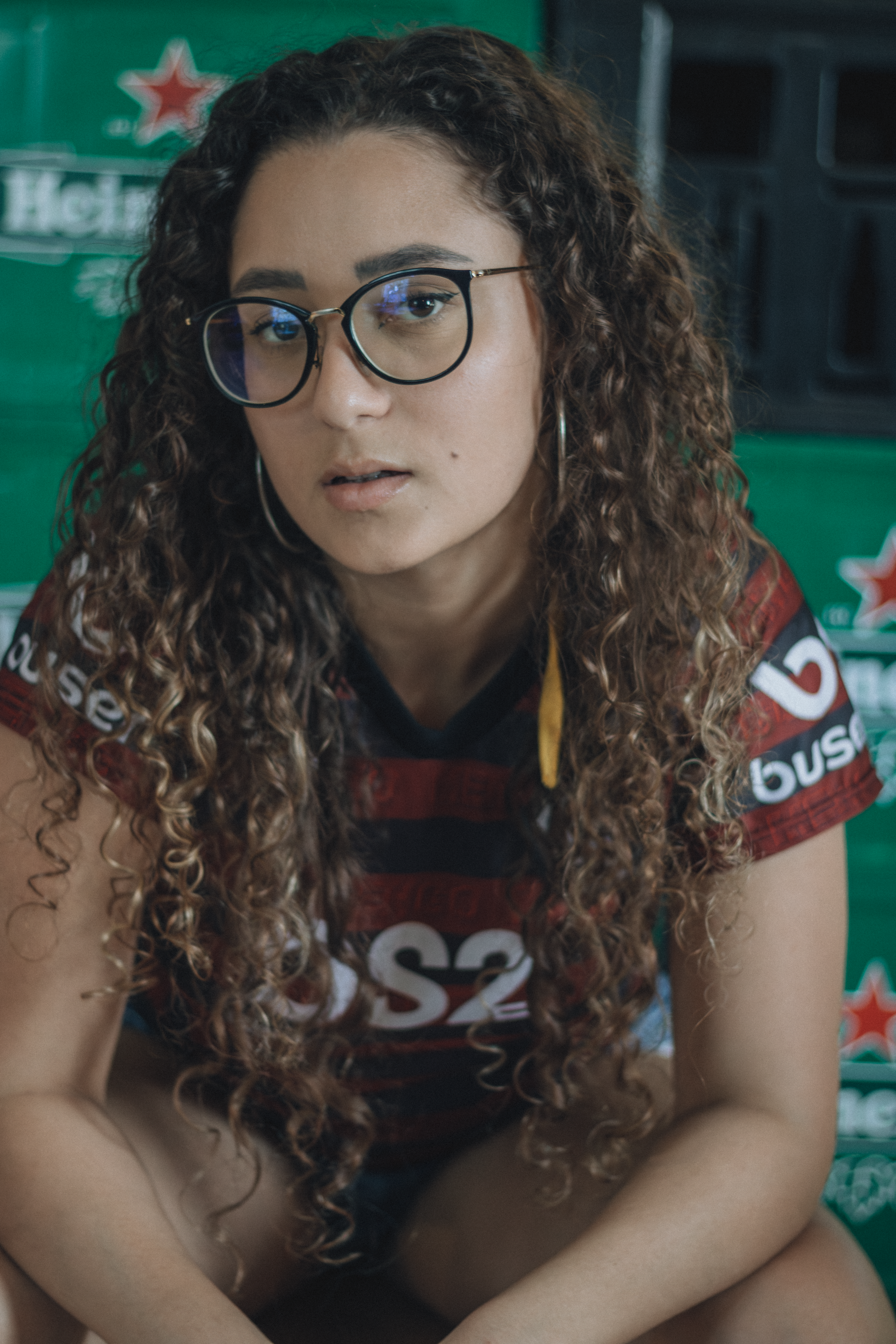 Portrait of a young woman with curly hair in a sports jersey in front of beer crates.