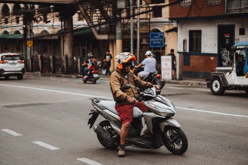 Free Adult male on scooter wearing helmet in busy city street during daytime. Stock Photo