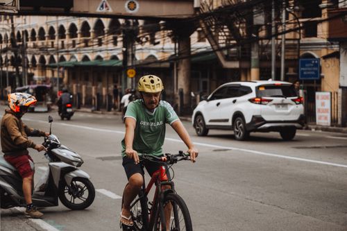 Free A cyclist wearing a helmet rides alongside city traffic in a bustling urban area street. Stock Photo