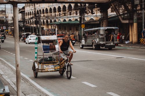 Free A man rides a tricycle on a busy street, capturing the vibrant city life. Stock Photo