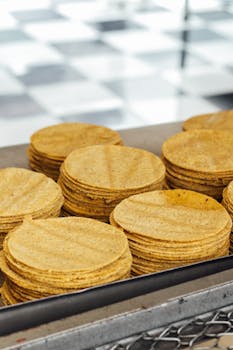 A close-up view of neatly stacked traditional corn tortillas in a bakery setting.