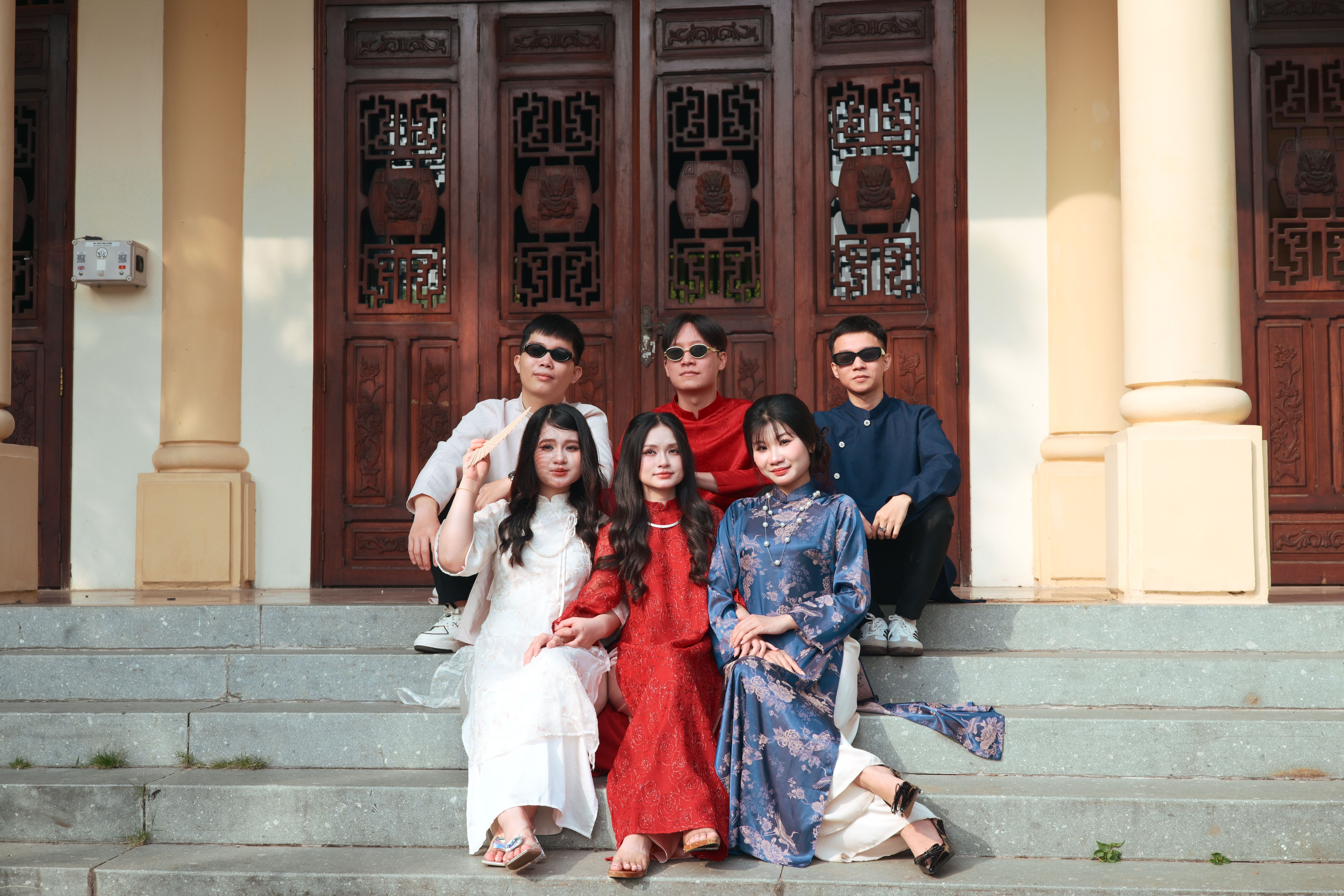 Group of friends posing in traditional attire on sunny steps.