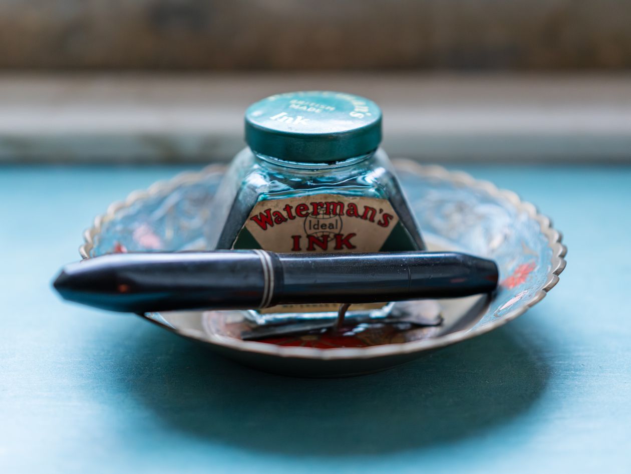 A vintage ink bottle alongside a fountain pen on a wooden surface — fountain pen bottled ink for beginners
