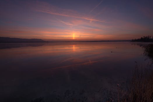 Peaceful sunrise view over a tranquil lake with a colorful sky reflecting on the water surface.