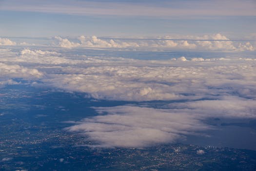 Captivating aerial view of fluffy clouds hovering over a landscape and water body during the day.