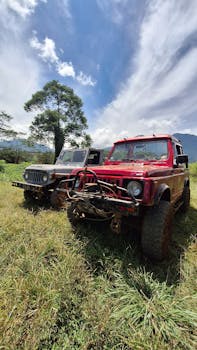 Red and silver Jeep parked outdoors under blue sky on grassy terrain.