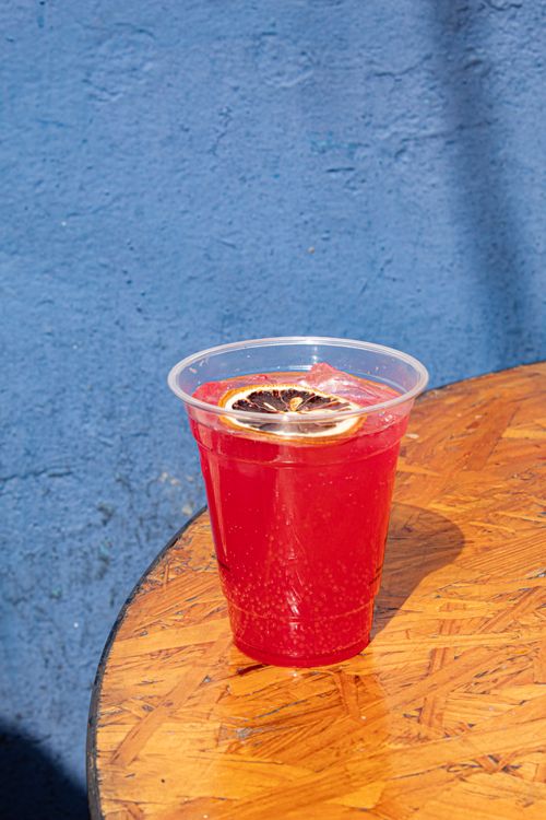 Free Plastic cup of hibiscus drink with lemon slice on wooden table by blue wall, outdoor setting in Mexico City. Stock Photo