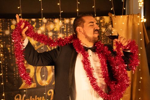 Free Man in formal wear celebrating with tinsel and wine at a festive event. Stock Photo