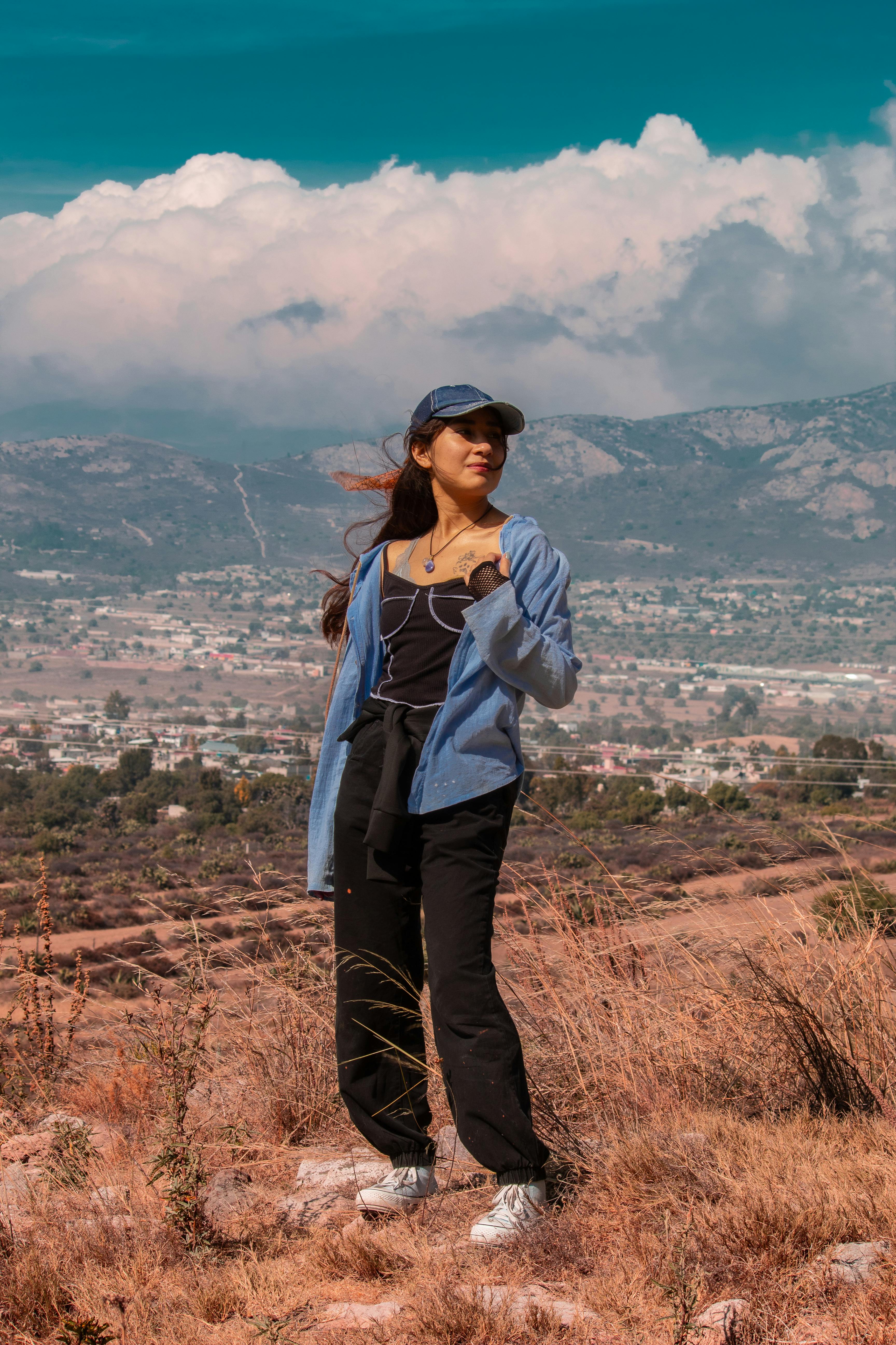 A young woman stands confidently with mountains and a scenic town backdrop in Hidalgo, Mexico.