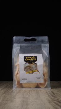 Close-up of Kerupuk Kemplang in a sealed bag on a wooden table with dark background. - Fotografer Sidoarjo