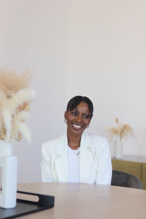 Free Stylish woman in white suit, smiling indoors in a minimalist setting with soft lighting. Stock Photo