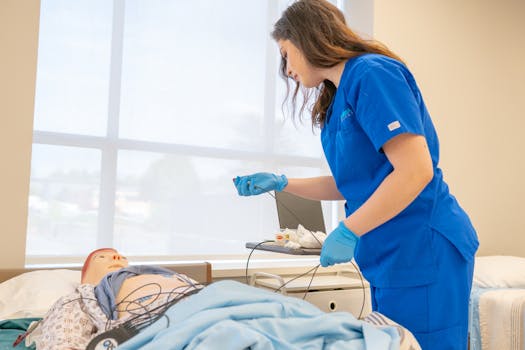 A nursing student in blue scrubs attends to a medical mannequin in a training room.