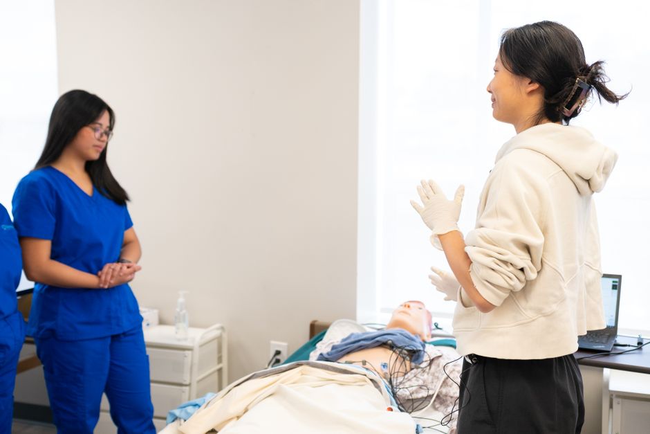 Nursing students engage in hands-on training with a medical dummy in a clinical setting.