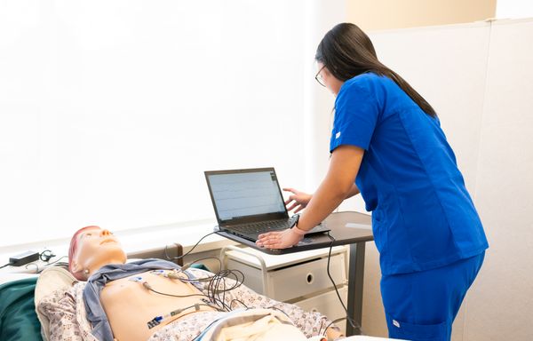 Nurse training with medical dummy and laptop in simulation lab