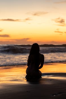 A serene silhouette of a woman sitting on a beach during a vibrant sunset in El Salvador.