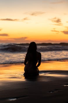 A serene silhouette of a woman sitting on the sandy beach during a stunning sunset in El Salvador.