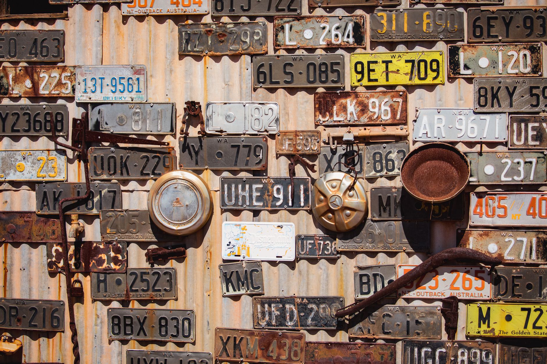 Collection of vintage license plates displayed on a corrugated metal wall in Leonora, Australia.