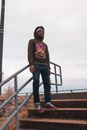 一个戴着墨镜和连帽衫的时尚男人，站在户外楼梯上，背景是多云的天空