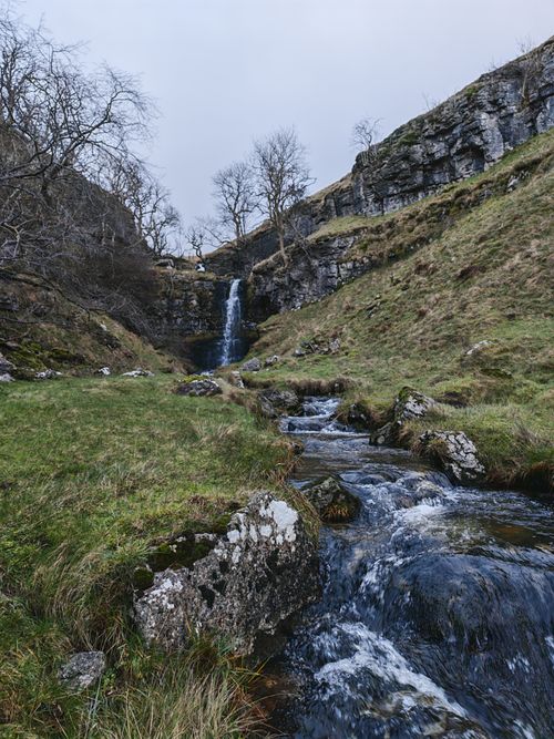 Free Tranquil waterfall cascading through rocky terrain in a peaceful mountainous setting. Stock Photo
