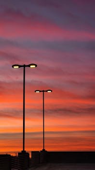 Silhouette of streetlights against a vibrant orange and purple sunset sky.