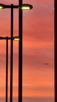 A serene cityscape with streetlights and an airplane silhouetted against a vibrant sunset sky.