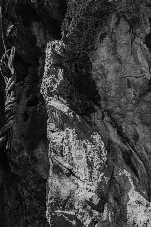 Free Detailed view of a rocky cliff in black and white, featuring a rugged rope. Stock Photo