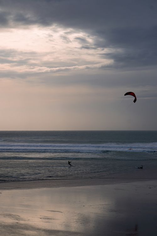 Free Kiteboarder gliding on ocean waves as the sun sets behind dramatic clouds. Stock Photo
