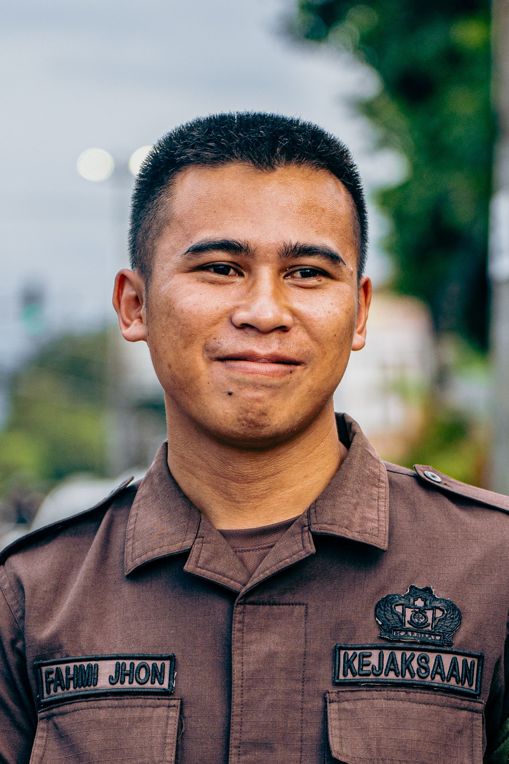 Close-up portrait of a smiling Indonesian security officer in uniform outdoors, showcasing pride and professionalism.